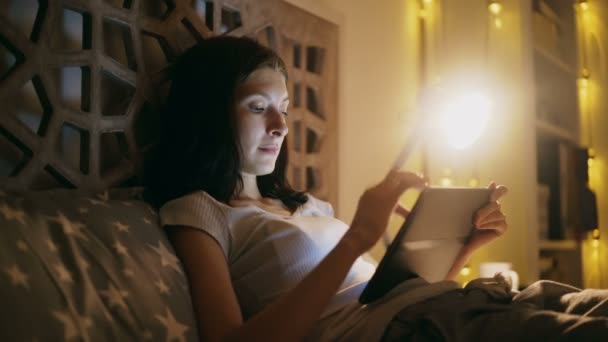 Jonge lachende vrouw met behulp van tablet pc voor online winkelen in bed liggen thuis 's nachts — Stockvideo