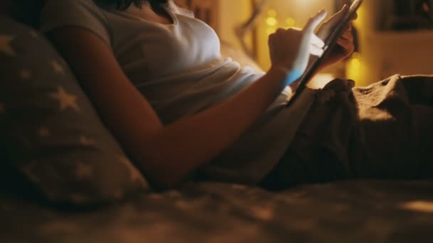 Inclinazione di felice donna sorridente utilizzando tablet computer sdraiato a letto a casa di notte — Video Stock