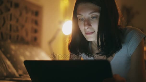 Close-up of young attractive woman using tablet computer at night time lying in bed at home — Stock Video