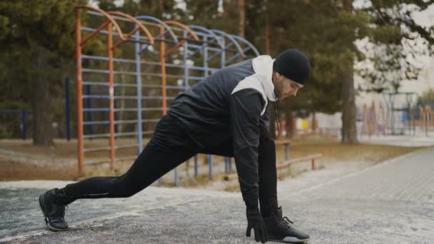 Ελκυστικά άνθρωπος δρομέας που κάνει το τέντωμα άσκηση, προετοιμασία για την πρωινή προπόνηση και τζόκινγκ στο πάρκο του χειμώνα — Αρχείο Βίντεο