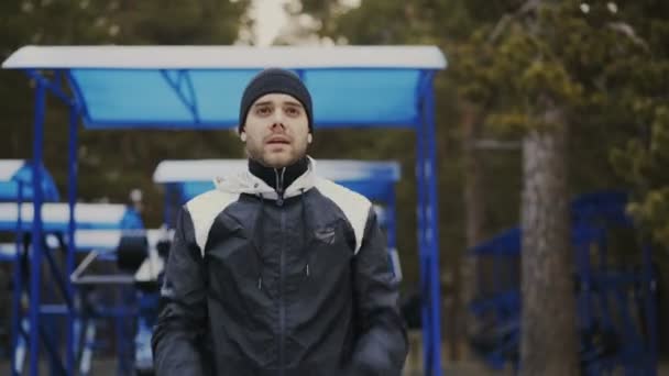 Молодий спортсмен робить розминку перед тренуванням в зимовому парку — стокове відео