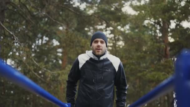 冬の公園屋外でバーの腕立て伏せ運動を行う若い選手男 — ストック動画