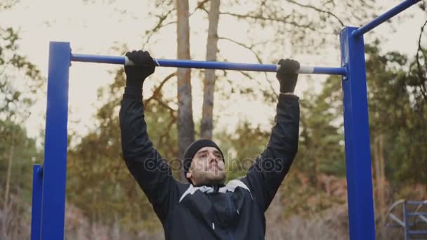 Sportieve jongeman doen pull-up oefening in winter park in openlucht — Stockvideo
