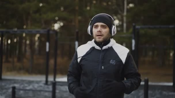 Homme attrayant dans les écouteurs faire de l'exercice d'échauffement se préparer pour le jogging tout en écoutant de la musique dans le parc d'hiver — Video