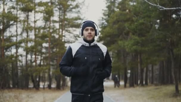 Mężczyzna atrakcyjny biegacz w słuchawkach joggingu podczas słuchania muzyki w parku zimowym w godzinach porannych — Wideo stockowe