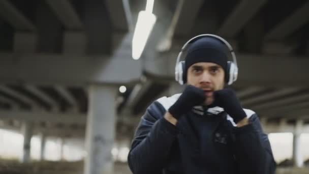 Zbliżenie śledzenia sprawny człowiek bokser w słuchawki robi ćwiczenia bokserskie w położenie w centrum miasta na zewnątrz w zimie — Wideo stockowe