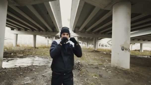 Dolly zoom disparo de boxeador hombre en los auriculares haciendo ejercicio de boxeo mientras escucha música en la ubicación urbana al aire libre en invierno — Vídeos de Stock