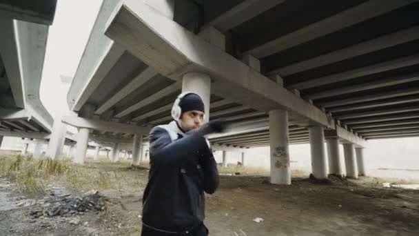 Rastreamento tiro de boxeador homem em fones de ouvido fazendo exercício de boxe enquanto ouvir música em localização urbana ao ar livre no inverno — Vídeo de Stock