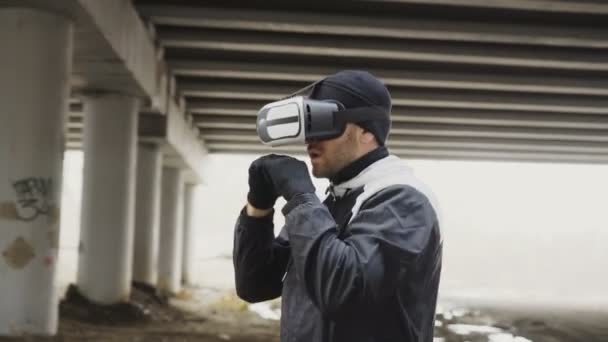 Tracking shot of boxing man in VR 360 headset training punches in virtual reality fight at urban location outdoor in winter — Vídeo de stock