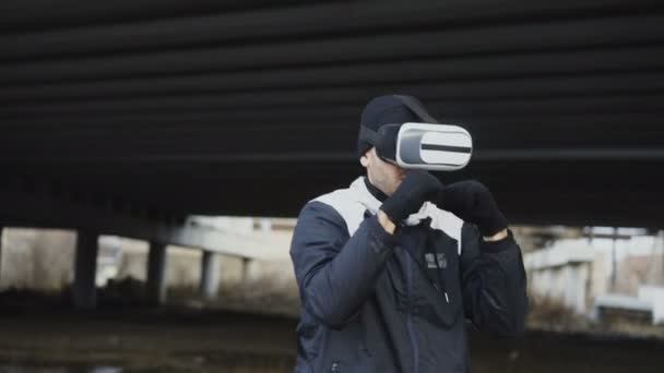 Tracking shot voor boksen man in Vr 360 headset opleiding stoten in virtuele werkelijkheid strijd op stedelijke locatie buiten in de winter — Stockvideo