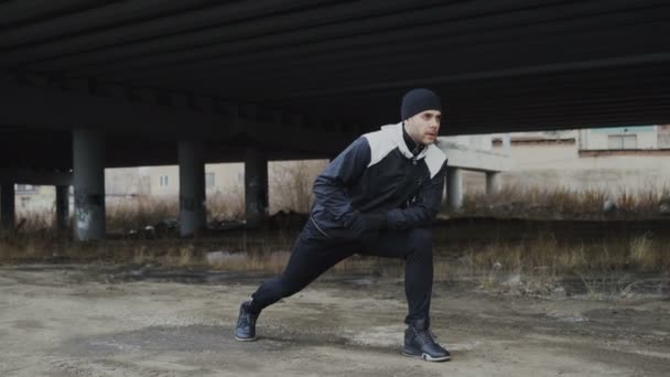 Runner atrakcyjny mężczyzna robi ćwiczenia rozciągające na treningu rano i jogging w miejscu miejski na zewnątrz w zimie — Wideo stockowe