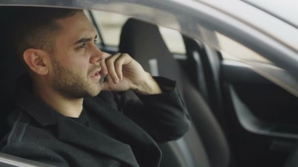 Крупный план стрессового бизнесмена, ругающегося и говорящего по телефону, сидящего в машине на улице — стоковое видео