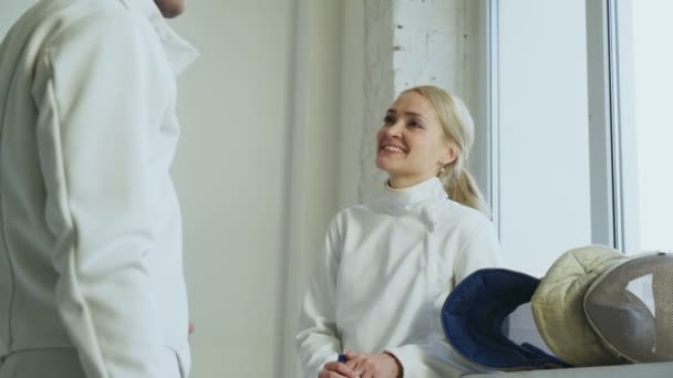 Dos jóvenes esgrimistas hombre y mujer hablando después del entrenamiento de esgrima en interiores — Vídeos de Stock