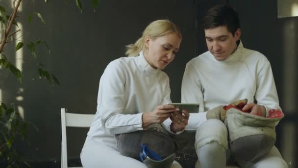 Dois jovens esgrimistas homem e mulher assistindo esgrima tutorial no smartphone e compartilhar experiência depois de treinar dentro de casa — Vídeo de Stock