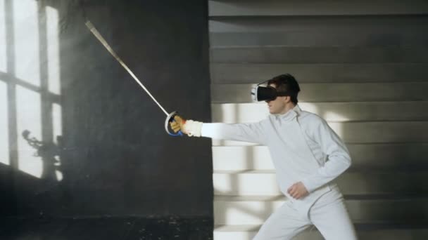 Концентрований фехтувальник практикує вправи з фехтування за допомогою гарнітури VR та тренувальної симулятор змагань гри в приміщенні — стокове відео