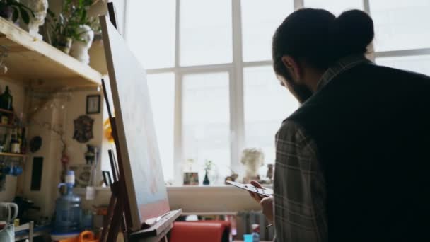 Skilled artist man teaching young woman painting on easel at art school studio - creativity, education and art people concept — Stock Video