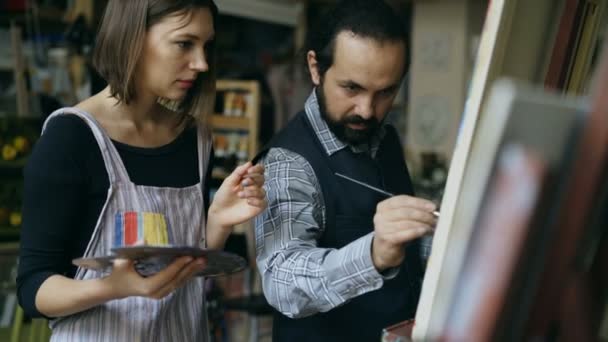 Rastreamento tiro de artista qualificado homem ensinando jovem a desenhar pinturas e explicando o básico no estúdio de arte — Vídeo de Stock