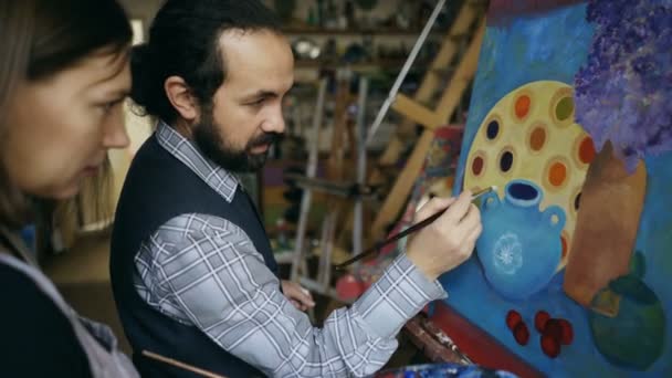 Képzett művész ember tanítási fiatal lány felhívni a festmények, és elmagyarázza az alapokat a művészeti stúdió — Stock videók