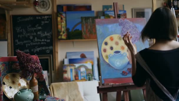 Achteraanzicht van de jonge schilder meisje in schort schilderij stilleven foto op canvas in de kunst-klasse — Stockvideo