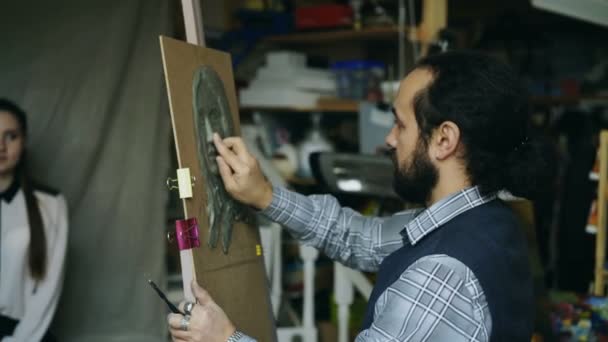 Escultor creando escultura de la cara de los seres humanos sobre lienzo mientras mujer joven posando para él en el estudio de arte — Vídeo de stock