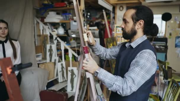 Geschickter Bildhauer arbeitet mit Knetmasse auf Leinwand, um Frauengesicht des posierenden Modells im Kunstatelier zu schaffen — Stockvideo
