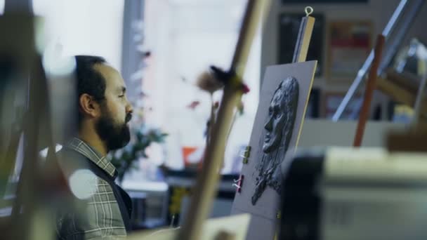アート スタジオでポーズをとる彼の女性と話しながらキャンバスに人間の顔の彫刻を作成する彫刻家 — ストック動画