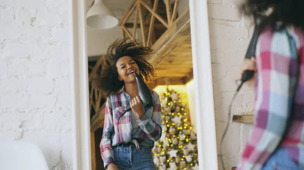 Curly funny african american girl dancing and singing with hair dryer in front of mirror at home — Stok Foto