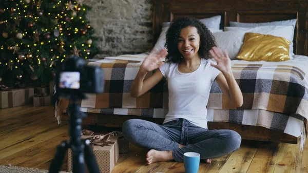 Молодая веселая смешанная расовая девушка записывает видео блог о упаковке рождественских подарочных коробок дома — стоковое фото
