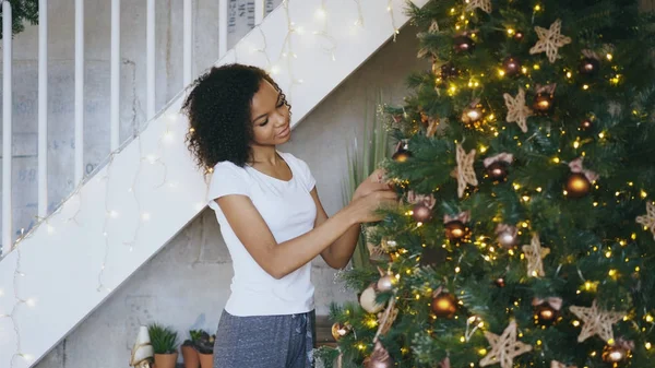 Curly menina de raça mista decorando árvore de Natal em casa se preparando para a celebração de Natal — Fotografia de Stock