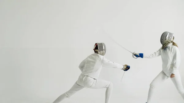 Young woman fencer having fencing training with trainer in white studio indoors — Stock Photo, Image