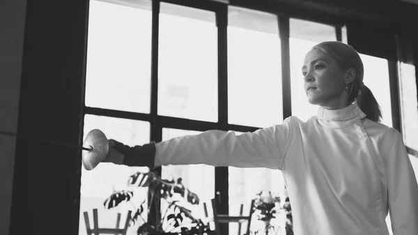 Jovem mulher esgrimista concentrada treinamento esgrima exercício em estúdio dentro de casa — Fotografia de Stock