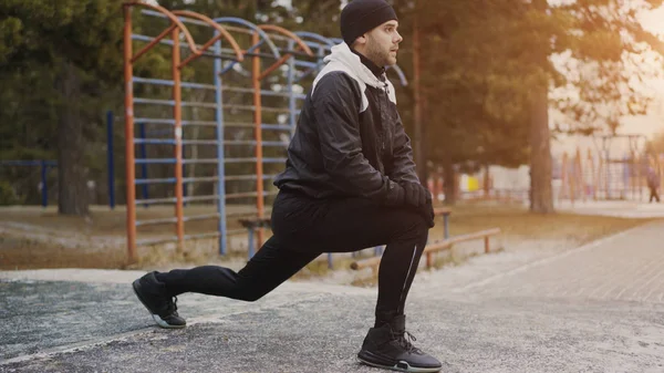 Atractivo corredor hombre haciendo ejercicio de estiramiento preparándose para el entrenamiento de la mañana y trotar en el parque de invierno — Foto de Stock