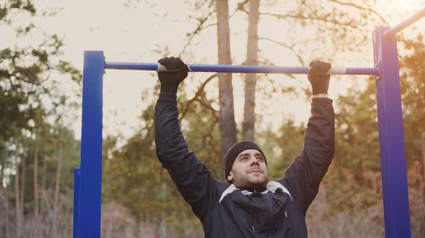 Hombre atlético joven haciendo ejercicio pull-up en el parque de invierno al aire libre — Foto de Stock