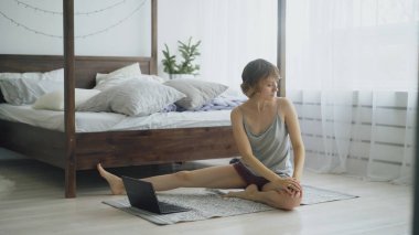 Yoga egzersiz yaparak ve dizüstü bilgisayar evde eğitmen dersi izlerken genç çekici kadın