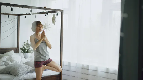 Fiatal gyönyörű nő csinálás jóga gyakorlás közel otthon hálószoba ágy — Stock Fotó