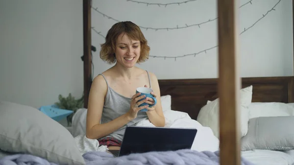 Attrayant femme gaie ayant chat vidéo en ligne avec des amis en utilisant une caméra portable tout en étant assis sur le lit à la maison — Photo