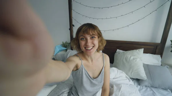 Fiatal vidám nő vesz használ smartphone ült az ágyban, az otthon selfie-portré — Stock Fotó