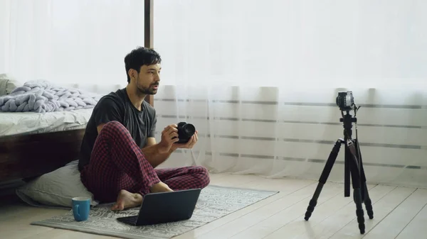 Homem bonito fotógrafo de gravação de vídeo blog sobre equipamentos de fotografia sentado perto da cama em casa — Fotografia de Stock