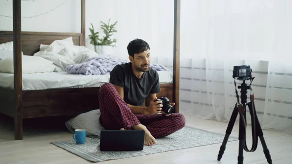 Bel homme photographe enregistrement vidéo blog sur la nouvelle caméra assis près du lit à la maison — Photo