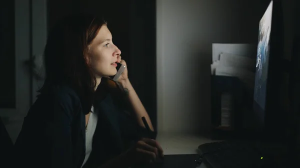 Konsantre kadın tasarımcı konuşurken telefon çalışma ofisinde gece işi bitirmek için bilgisayar ve grafik tableti kullanarak — Stok fotoğraf