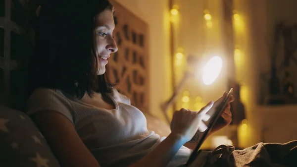 Boldog mosolygó nő részére cserépdarab a szociális média ágyban fekve, otthon éjjel tabletta számítógép segítségével — Stock Fotó