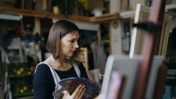 年轻女艺术家在围裙绘画图片在帆布在艺术工作室 — 图库照片