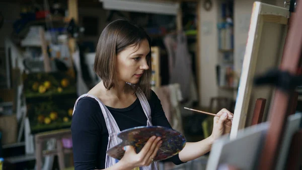 Jeune femme artiste en tablier peinture tableau sur toile en atelier d'art — Photo