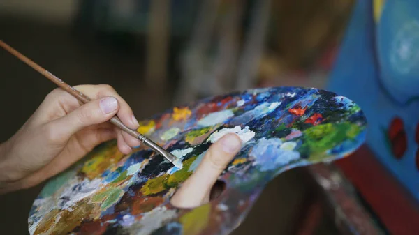 El primer plano de las mujeres mezclan a mano las pinturas con el pincel en la paleta en la clase artística —  Fotos de Stock