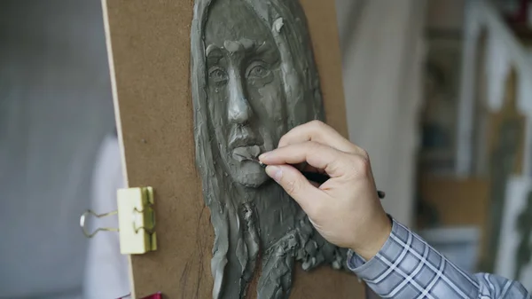Крупный план скульптора, создающего скульптуру человеческого лица на холсте, в то время как молодая женщина позирует ему в художественной студии — стоковое фото