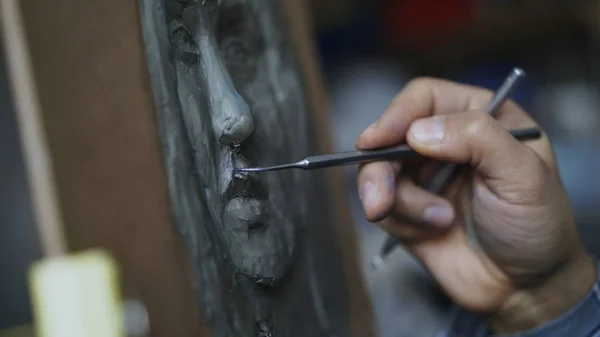 Крупный план скульптора, создающего скульптуру человеческого лица на холсте в художественной студии — стоковое фото