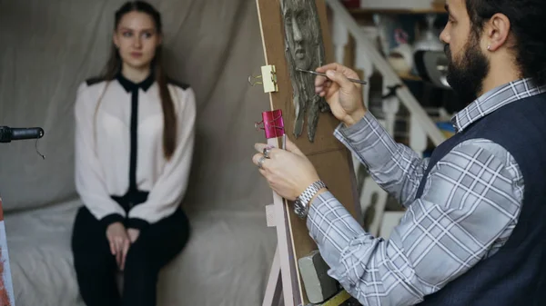 Szobrász létrehozása emberi arc szobra, vászon, míg a fiatal nő pózol neki művészeti stúdió — Stock Fotó