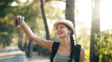 Genç turist kız backpacker şapka online video smartphone ile yaz ormanda yürüyüş sırasında sohbet içinde