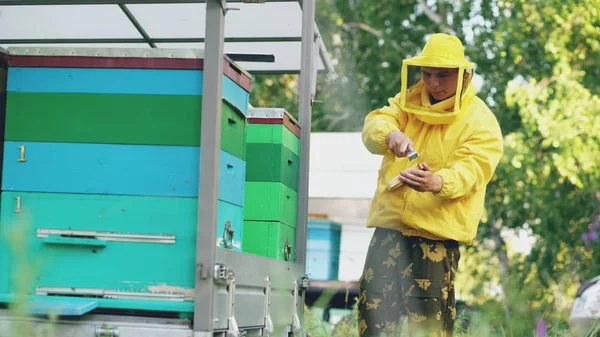 Joven apicultor hombre limpio marco de miel de madera trabajando en el colmenar en el día de verano —  Fotos de Stock