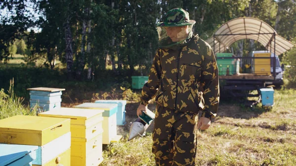 Joven apicultor fumando abejas lejos de la colmena en el colmenar —  Fotos de Stock